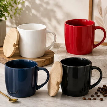 Four ceramic mugs in white, red, navy blue, and black, each paired with a small round wooden lid, arranged on a light ston...